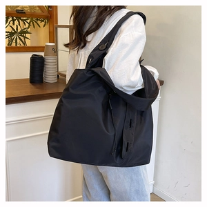Close-up of black nylon tote bag on shoulder showing wide strap and waterproof texture