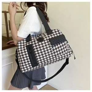 Detail of houndstooth travel bag showing adjustable nylon shoulder strap and zip pocket
