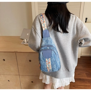 Detail of light blue denim chest bag with colorful floral embroidered wide shoulder strap