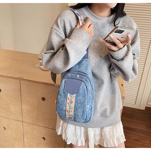 Detail of light blue denim crossbody bag featuring floral embroidery and adjustable strap