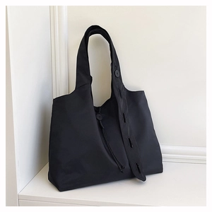 Close-up of black nylon tote bag featuring unique button strap detail on minimalist fabric