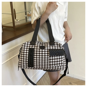 Detail view of large houndstooth travel bag showing black leather front pocket and strap