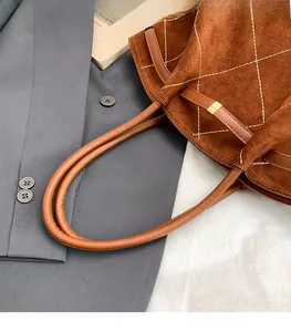 Close-up of brown suede tote bag featuring white diamond stitching and round handle
