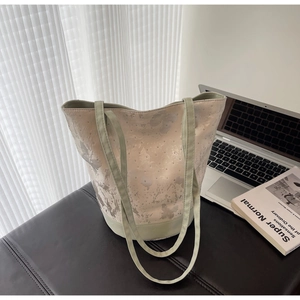Detail of light green bucket bag with silver rivet accents on a minimalist desk