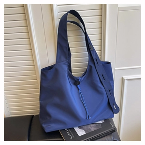 Detail of navy nylon tote bag with drawstring and adjustable button strap on bench
