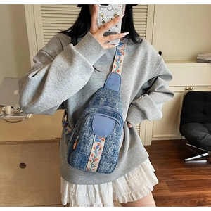 Detailed close-up of blue denim chest bag with colorful ethnic floral embroidery and zippers