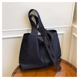 Detail of black nylon tote bag featuring wide adjustable strap and side drawstring design
