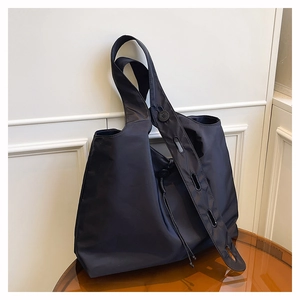 Detail of black nylon tote bag with drawstring side on a brown acrylic table