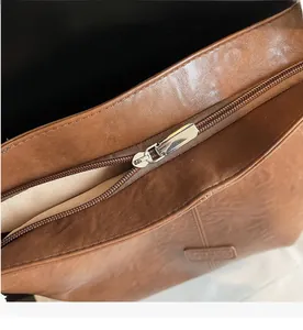 Close-up of smooth silver metal zipper and brown faux leather texture on tote bag