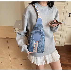 Detail of blue denim crossbody bag with colorful floral embroidered shoulder strap
