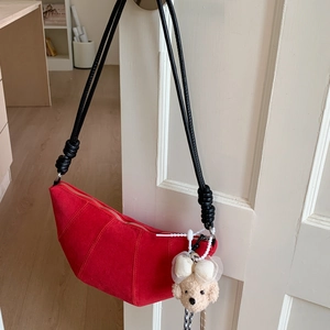 Détail du sac croissant en daim rouge avec bandoulière noire nouée et breloque chien mignon
