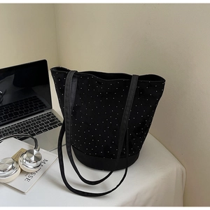 Detailed view of a black canvas bucket bag with white studs and long shoulder straps