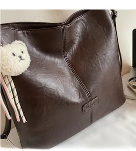 Detail of dark brown vintage faux leather tote bag with soft texture and plush bear charm