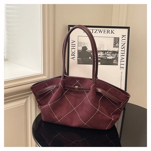 Detail of burgundy suede tote bag featuring white contrast stitching and gold hardware