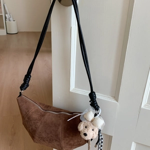 Détail du sac croissant en daim marron foncé avec coutures et breloque ours