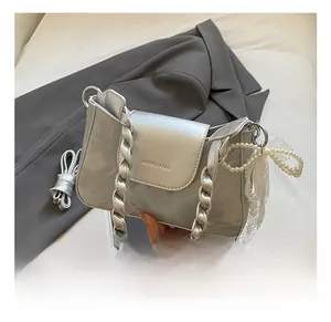 Detail of silver crossbody bag with twisted handle, pearl lace charm and metallic finish