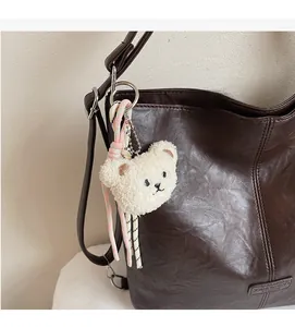 Close-up of a white plush bear charm with woven lanyard on a brown leather tote bag