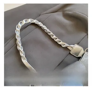 Detailed close-up of a metallic silver handbag with a twisted handle on grey fabric