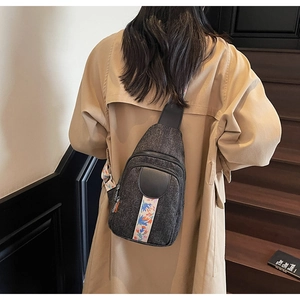 Detail of dark denim crossbody chest bag with colorful floral strap on beige trench coat