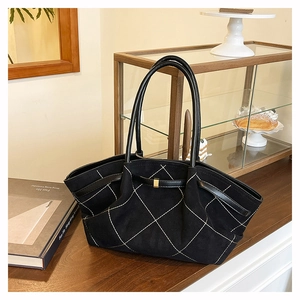 Detail of black quilted shoulder bag with white diamond stitching and gold buckle accents
