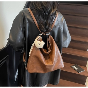 Detailed back view of vintage brown PU leather tote bag with plush bear charm on stairs