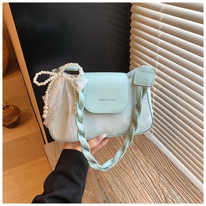 Detail of mint green shoulder bag featuring a woven strap and pearl bow decoration