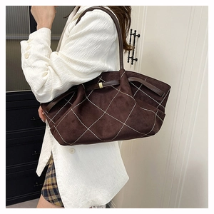 Close-up of suede tote bag featuring white quilted stitching and leather shoulder strap