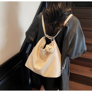 Detail view of cream white faux leather backpack with plush bear charm on wooden steps