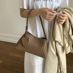 Dettaglio di una borsa baguette in pelle intrecciata marrone con trama e ciondolo
