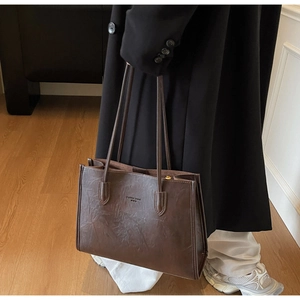 Detailed view of deep brown tote bag with vintage texture on long black coat
