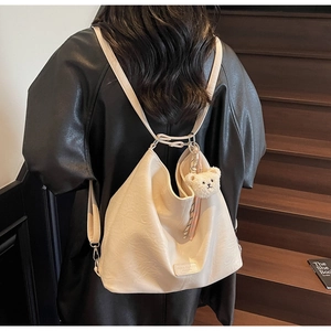 Detail view of cream faux leather tote with plush bear charm and striped scarf accent