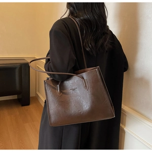 Close-up of a large dark brown tote bag with vintage leather texture on a black coat