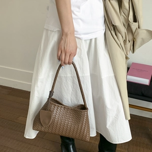 Dettaglio ravvicinato di una borsa in pelle intrecciata marrone abbinata a un trench