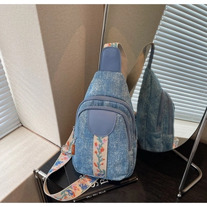 Detail of light blue denim crossbody bag with colorful floral ethnic woven zipper straps