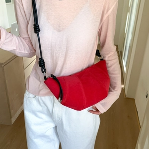 Détail du sac croissant en daim rouge avec coutures décoratives et bandoulière noire nouée