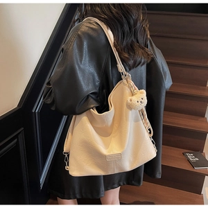 Detail of a creamy white retro tote bag with embossed texture and a bear charm on a model