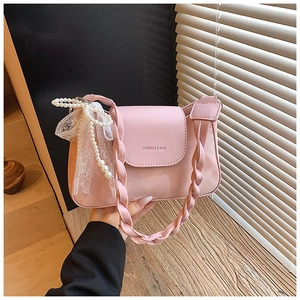 Detail of pink glossy handbag with woven strap, pearl chain, and lace bow charm