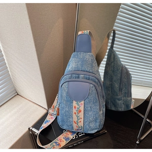 Detail of light blue denim crossbody bag with colorful floral embroidered strap and zipper