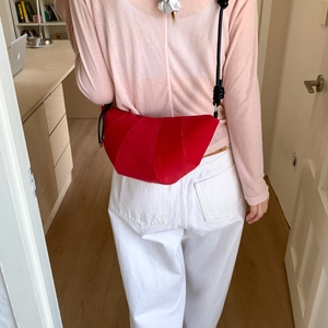 Détail du sac croissant en daim rouge avec bandoulière nouée porté par un mannequin