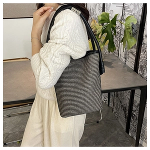 Detail of woven bucket bag featuring black and white texture and leather strap on model