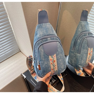Detail of blue denim sling bag with embroidered floral strap and vintage wash texture