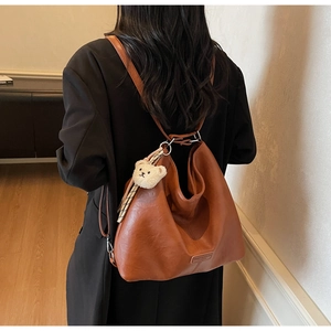 Detail view of brown faux leather tote bag with plush bear charm and silver metal hardware
