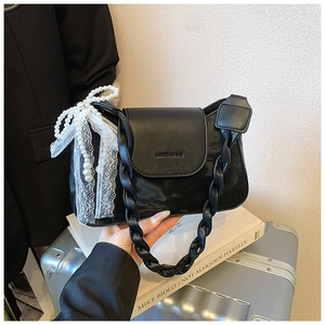 Detail of black leather bag with braided handle and white pearl ribbon bow decor