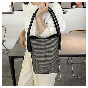 Close-up of woven bucket bag featuring black and white textures and leather handle