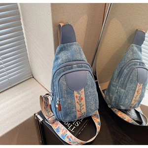 Detail of blue denim crossbody bag featuring ethnic floral embroidery strap and multi-zipper pockets