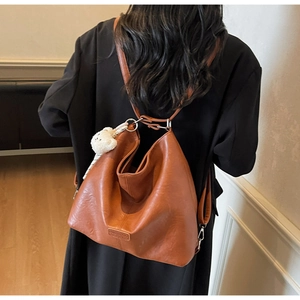 Back view of model carrying a large brown leather tote backpack with a cute bear charm