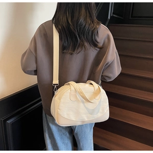 Canvas shell-shaped bag shown as a crossbody on a model with beige fabric straps