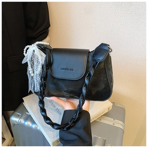Detail of black leather underarm bag with woven strap and pearl lace bow charm decoration