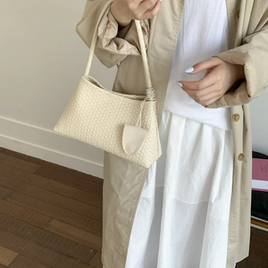Dettaglio della trama intrecciata della borsa color crema con mini ciondolo abbinato