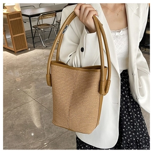 Close-up of beige woven bucket bag with long brown leather straps in a cafe setting